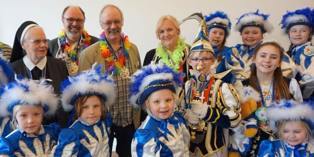 Viele Kinder in Karnevalsoutfit mit einigen weiteren Erwachsenen hinter ihnen. 