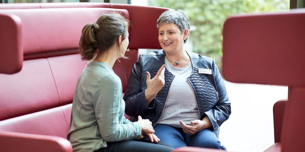 Zwei Frauen sitzen auf einem großen Sesselsofa und unterhalten sich angeregt. 